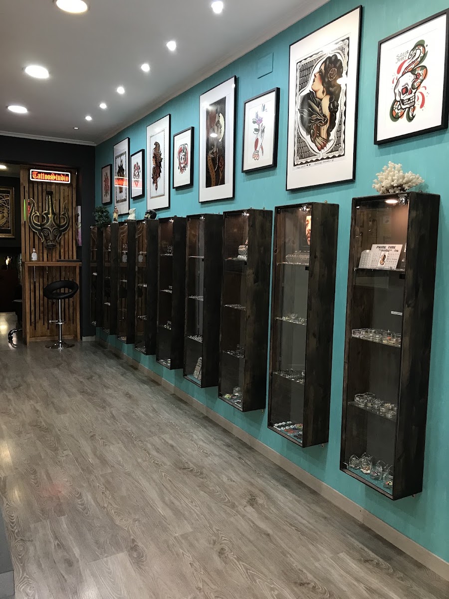 Pasillo del estudio: pared turquesa con láminas enmarcadas en negro y vitrinas de madera oscura con joyería, suelo de laminado gris.